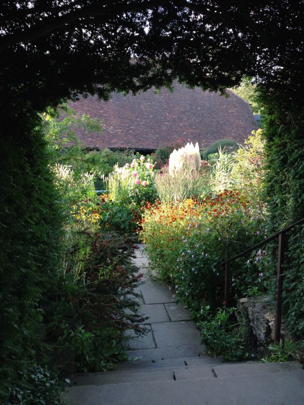 Looking through an archway to sun hitting the exuberant grasses and perennials
