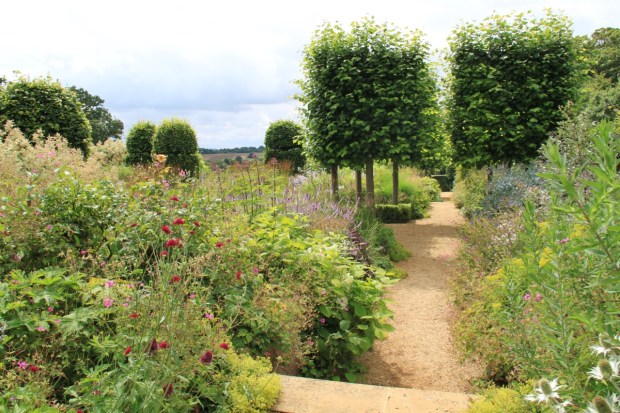 Soft, overflowing borders are broken up with pleached lime tree platforms at Broughton Grange